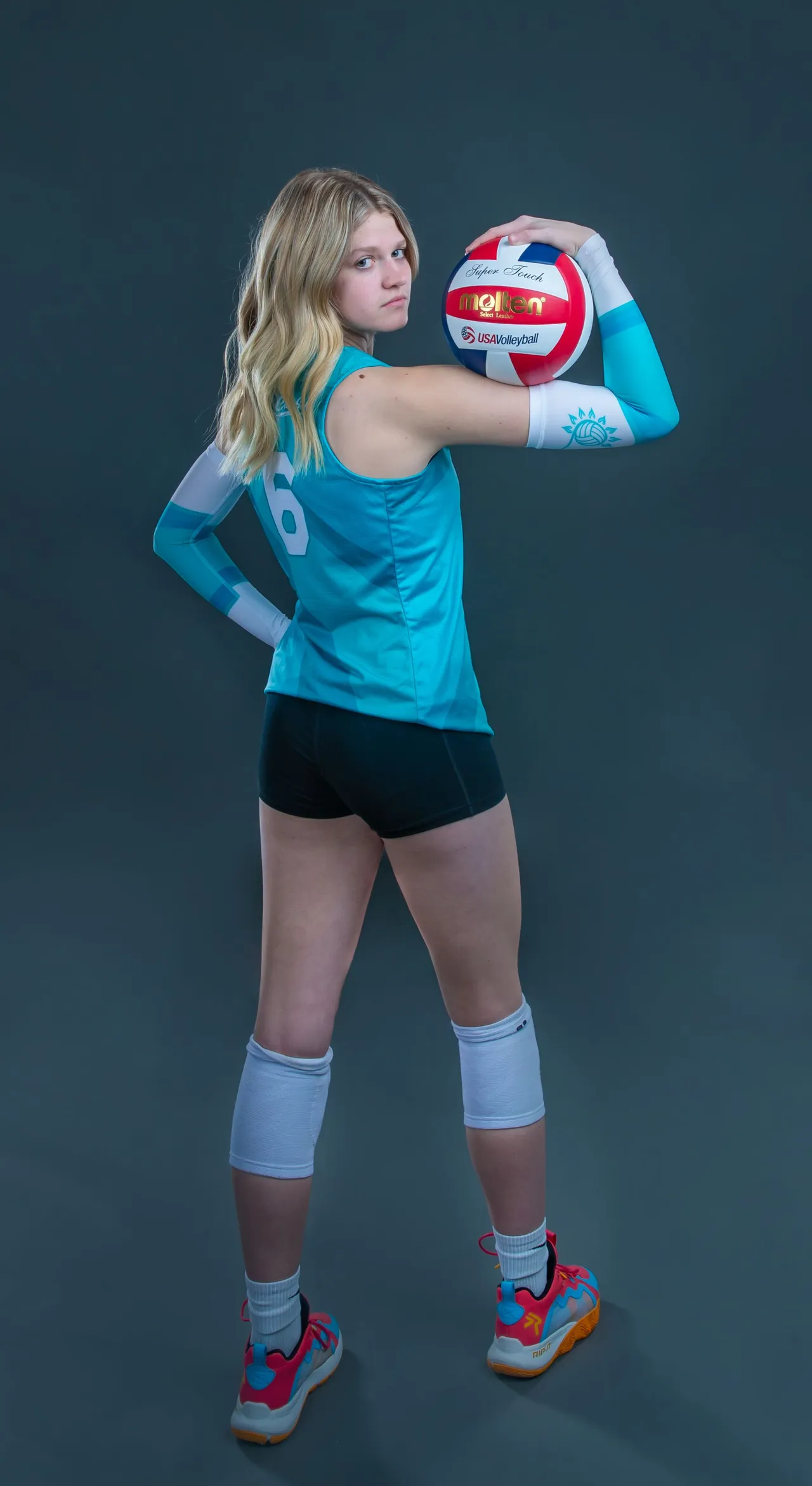 Athlete in turquoise volleyball gear holds a red-white ball against a dark background.