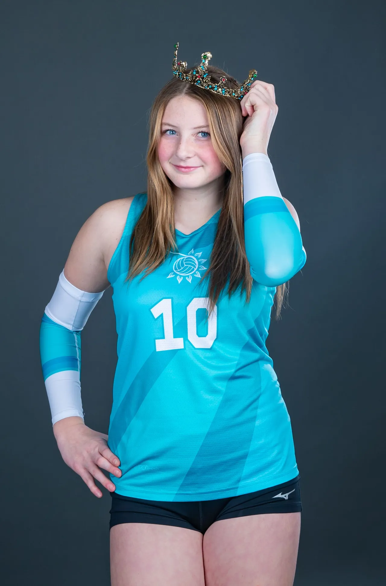 Athlete in turquoise jersey and arm sleeve, holding a crown and smiling against a dark background.