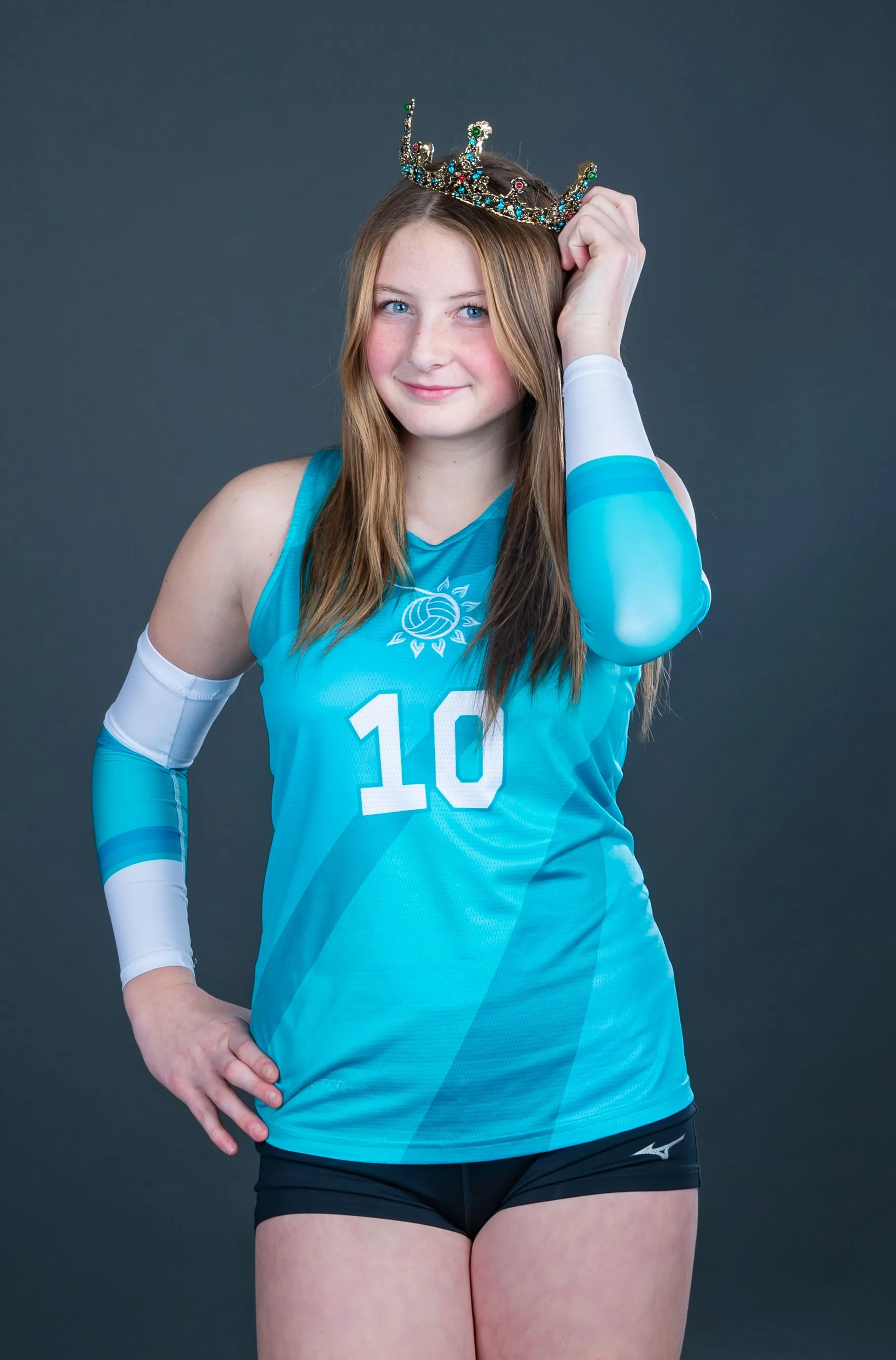 Athlete in turquoise jersey and arm sleeve, holding a crown and smiling against a dark background.