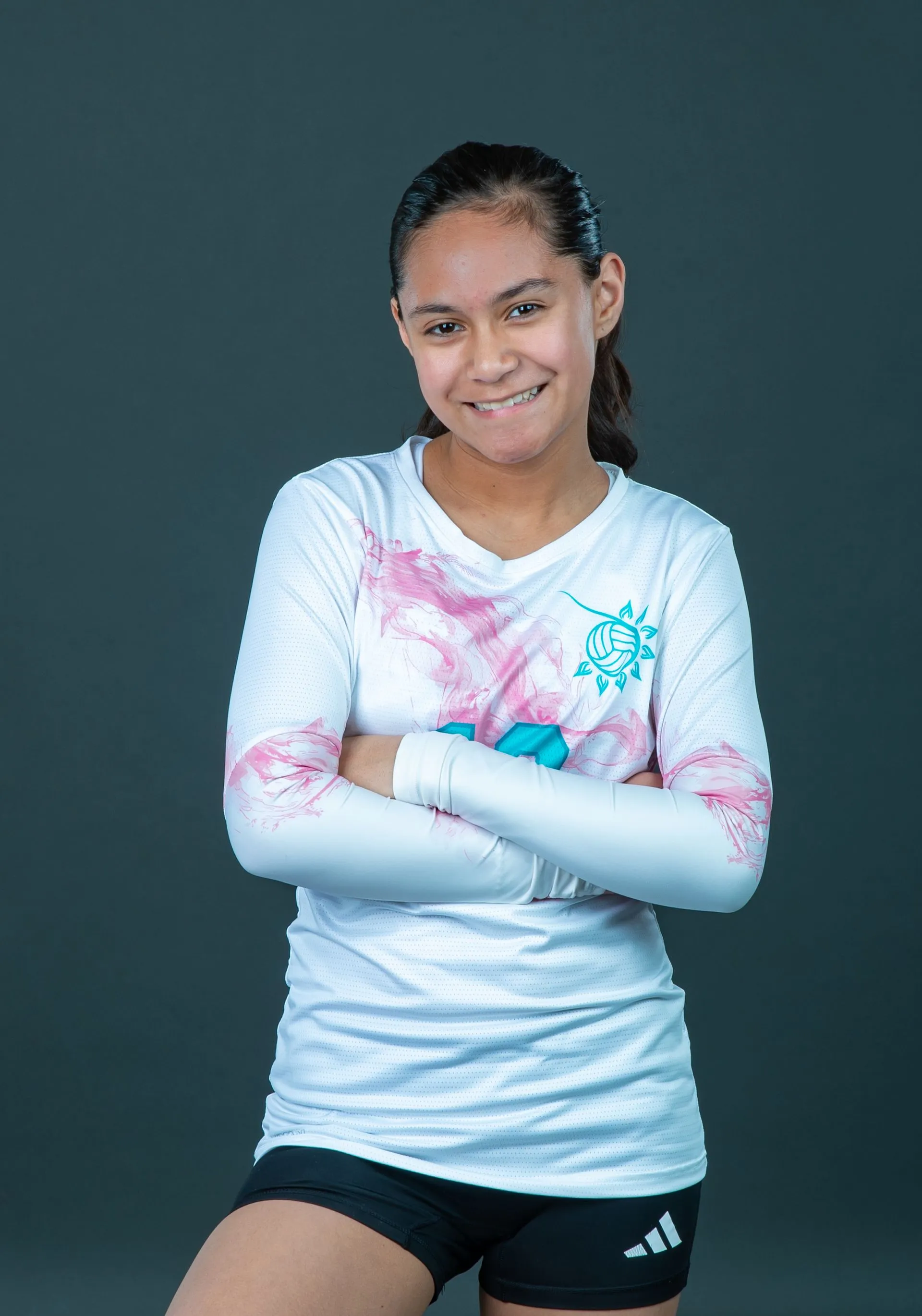 Person in a white shirt with pink accents, arms crossed, smiling against a dark background.