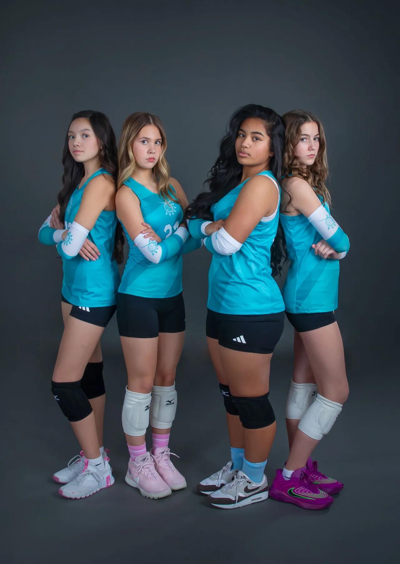 Four volleyball players in teal jerseys pose with crossed arms against a dark studio backdrop.