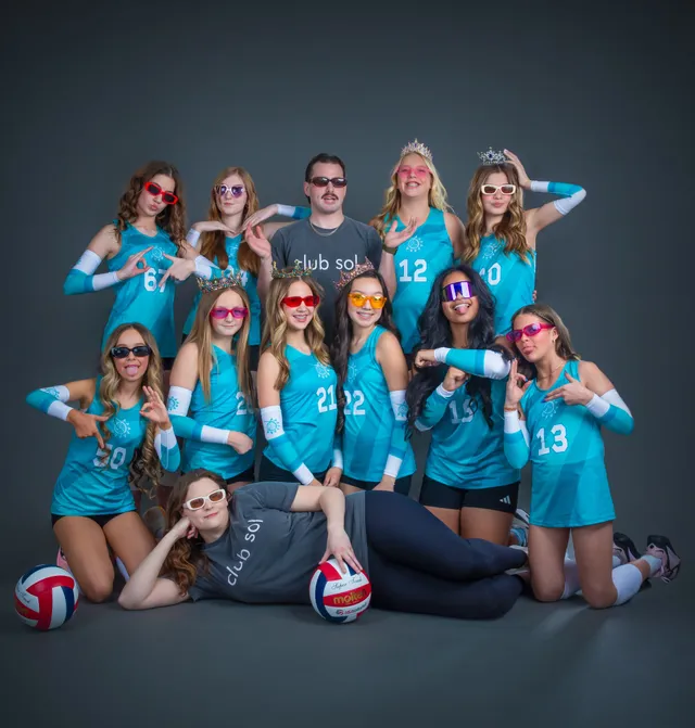 Volleyball team posing in teal jerseys with two volleyballs on a studio gray background